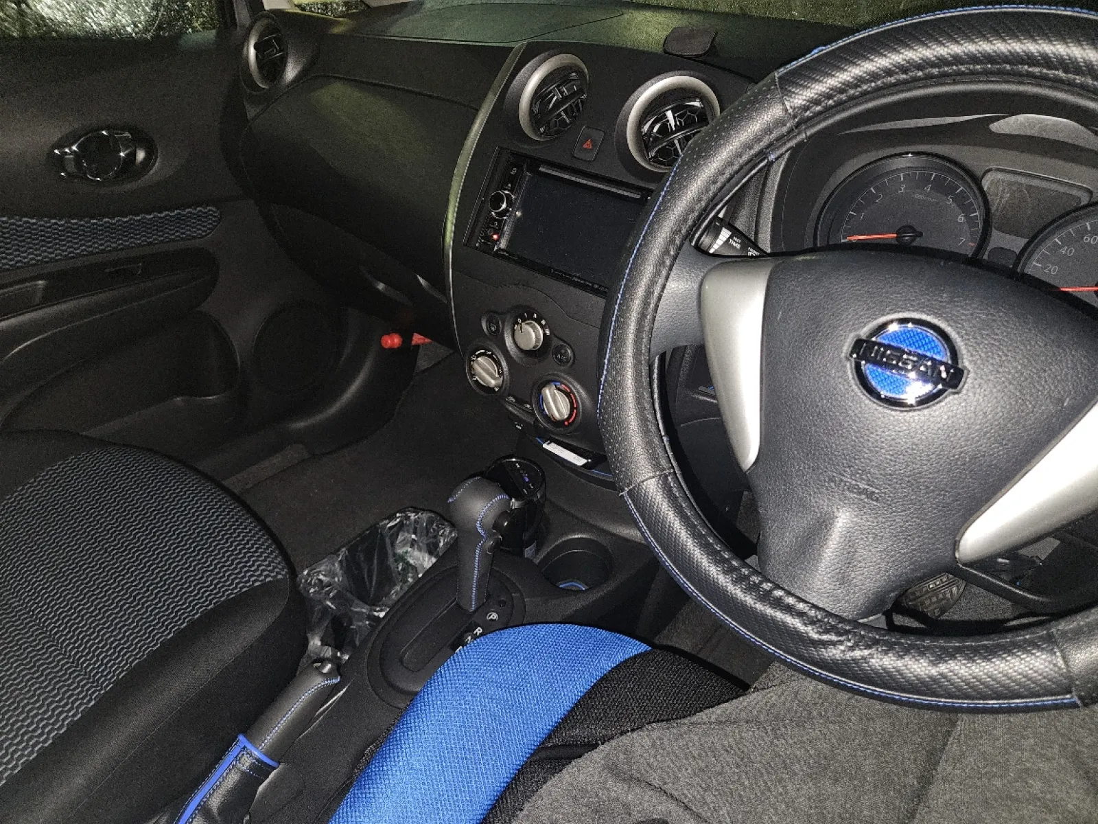 社外ナビとETCとプラズマクラスター、それから写真には収まってないですが運転席側にレーダーが購入時に既に付いていました。
車内は何か施さないと営業車もしくはレンタカー感が丸出しだったのでどうしようかな…と考え、純正シートが青い模様が入っていた為、青カラーで統一しました。
ハンドルカバー、エンブレムシール、シフトノブカバー、サイドブレーキカバー、運転席側のみシサポートクッション、ラバーマットが青ですね。
シフトノブカバーは自分で縫っていくタイプなのと裁縫も苦手なのも相まって、取り付けに3時間ほど掛かり一番苦労しましたが完成時の喜びもひとしお。
サイドブレーキカバーもレバー側は内側に滑り止めが施されてたので凄く固くて入りにくく、スカートの方も間にはまらなくてセンターコンソールごと浮かそうか悩むぐらい大変でした…
あとはこれも写真に収まってないですがシートベルトカバーと、目立たない様に黒いゴミ箱
そんなところでしょうか。