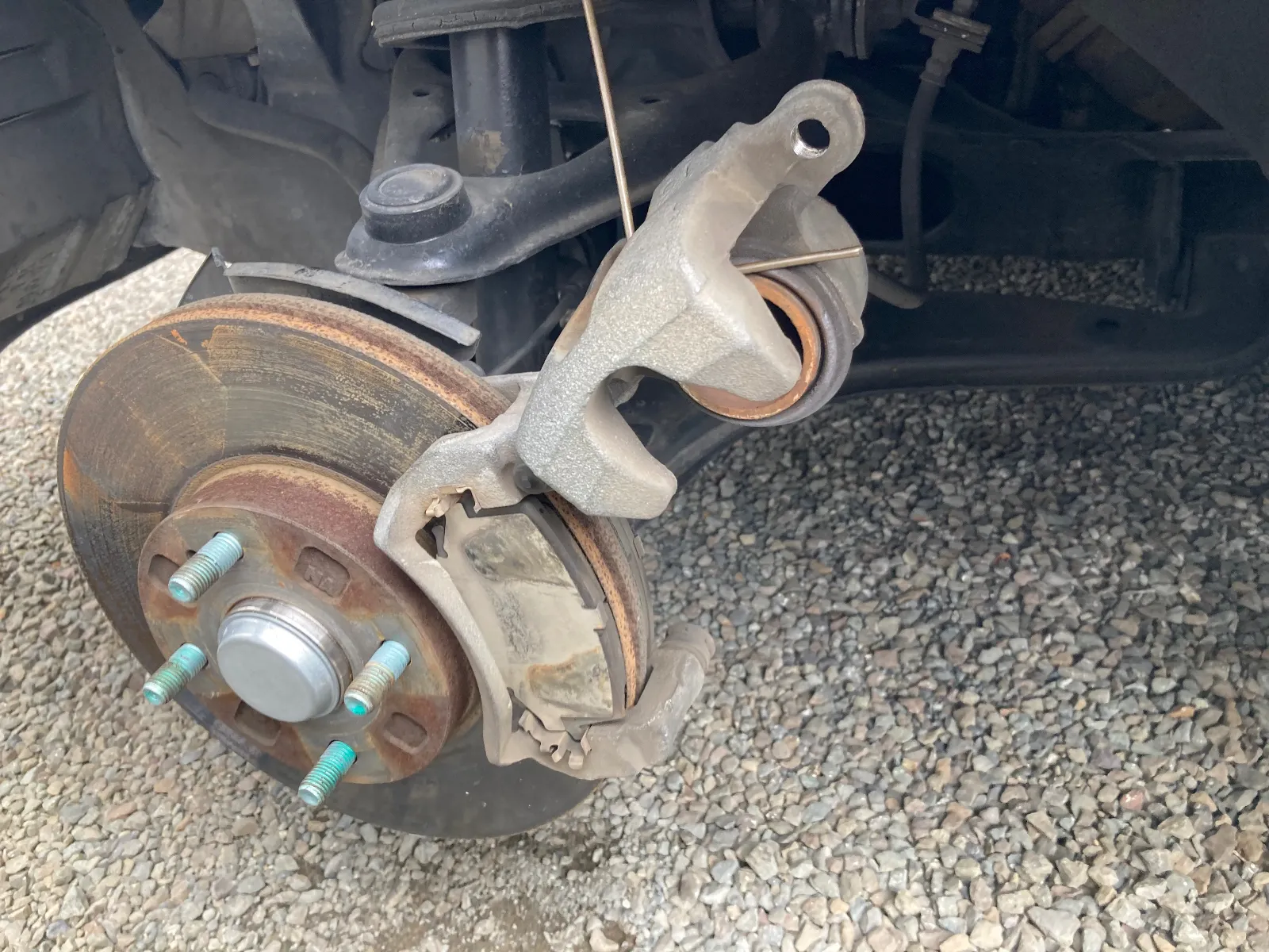 一輪づつ車載のパンタジャッキを使って、タイヤを外しての作業になります。ピストンシリンダーのユニットの下側のシャフトボルトを外して、持ち上げます。仮止めには針金がわりのありあわせの3mm銅パイプの切れ端を使いました。