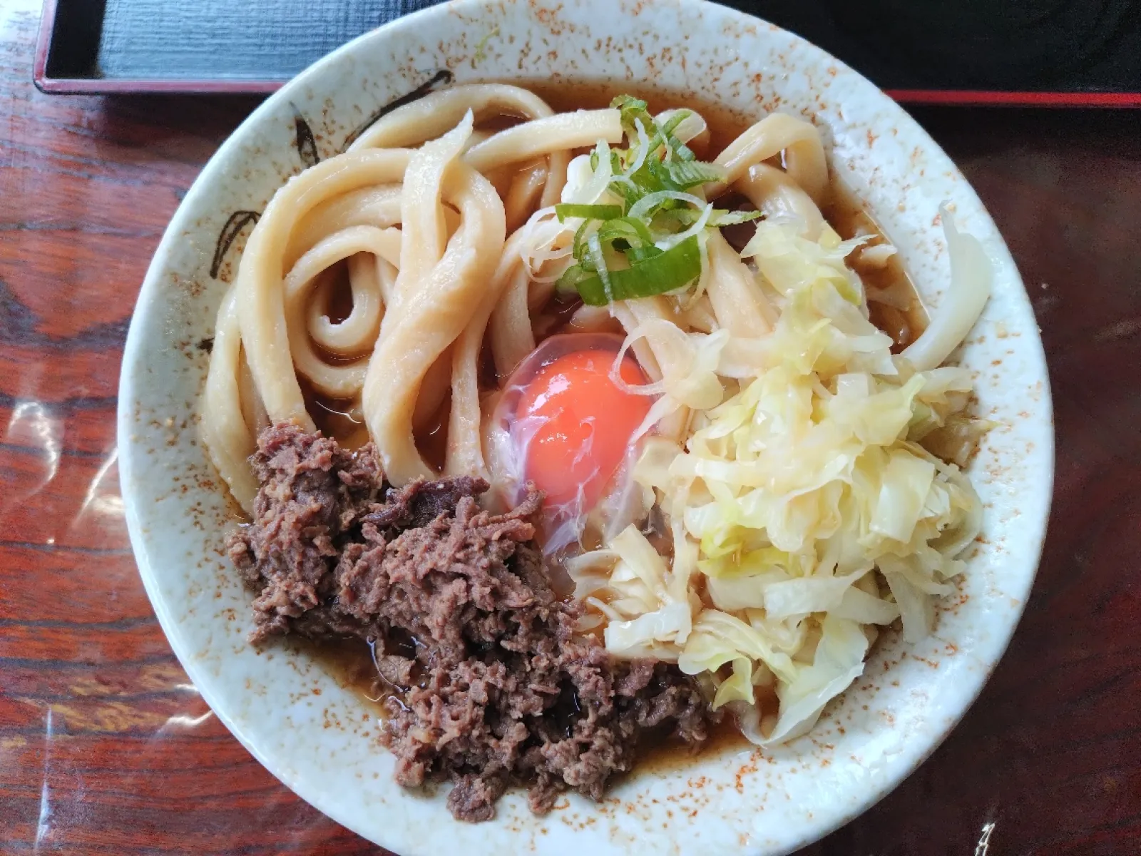 吉田うどんの名店です。
コロナ禍は個別に小皿わけだった、すりだね（辛い自家製七味みたいなもの）と天かすがテーブルで自由に取れるようになりました。
肉は馬肉です。ゆでキャベツはどのうどんにも付いてきます。
写真は肉玉うどん（1.5玉）